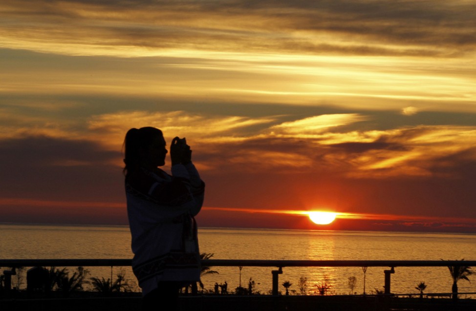 Woman takes a picture outside the Bolshoy Ice Dome as the sun sets on the Black Sea at the 2014 Sochi Winter Olympics
