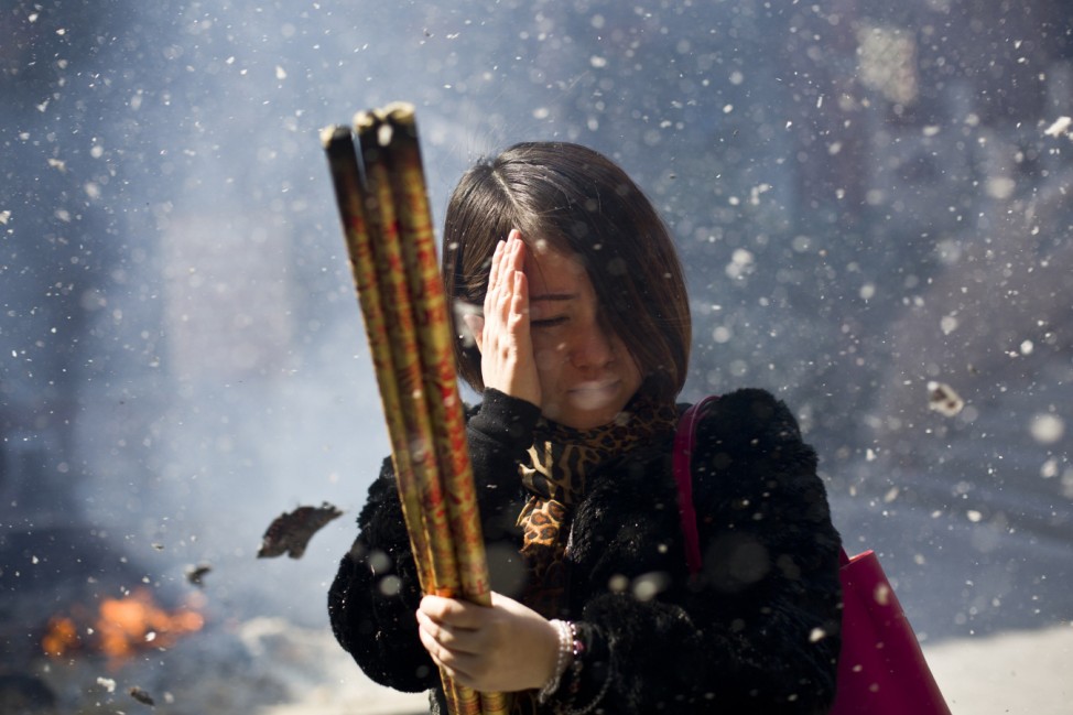 A woman dodges ash as she burns incense for good fortune on the Chinese Lunar New Year at a Taoist temple in central Shanghai