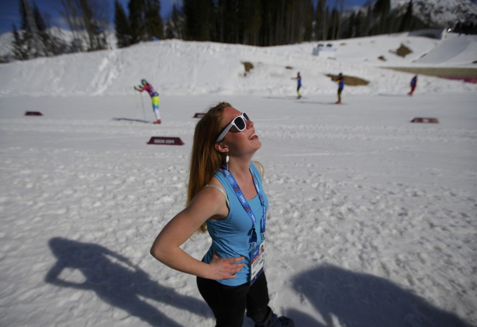 Staff member enjoys the sun as she waits for the start of the men's 15 km cross-country classic event at the Sochi 2014 Winter Olympic Games in Rosa Khutor