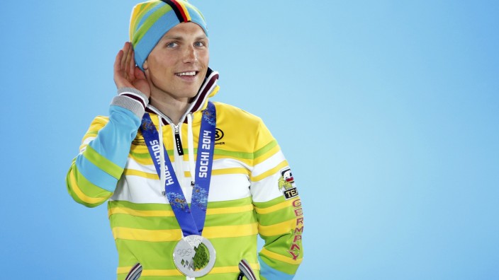 Silver medallist Germany's Lesser cups a hand around his ear to hear applause during victory ceremony for men's biathlon 20km individual event at 2014 Sochi Winter Olympics