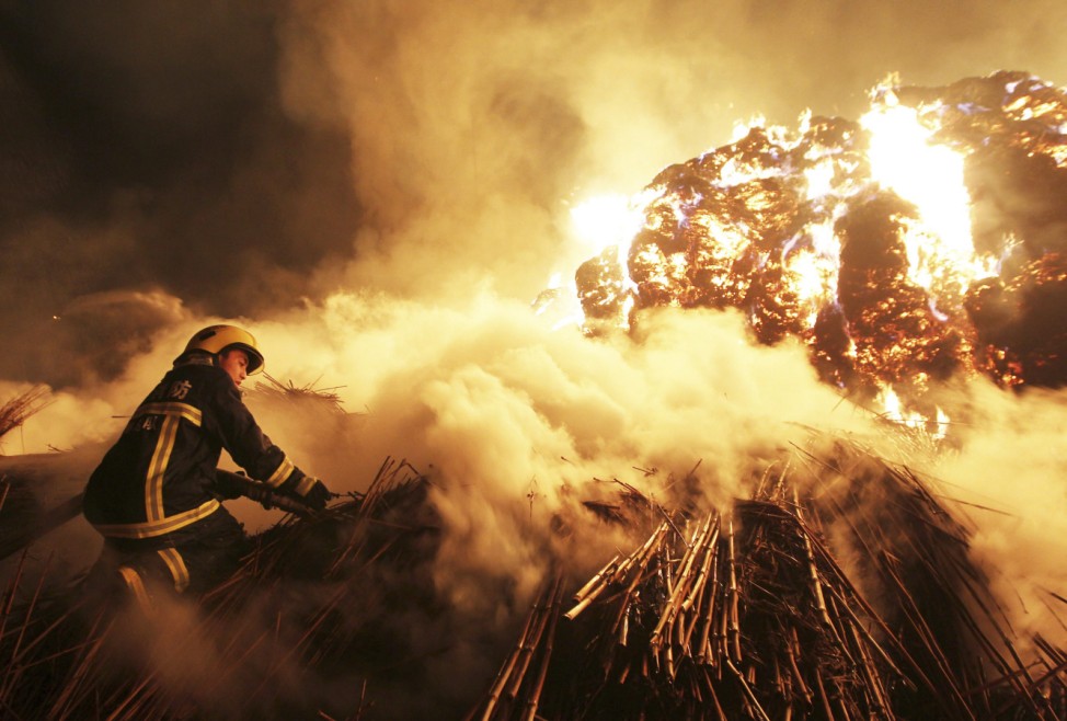 A firefighter attempts to extinguish a fire which broke out on piles of reed at a paper factory in Changde