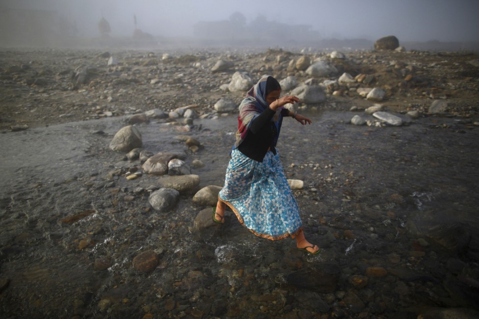 A women jump to reach a rock as she crosses Chepay River at Sapay, Achham