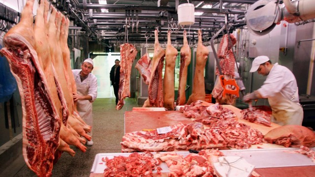 Butchers handle pig carcasses in a slaughterhouse in Mannheim