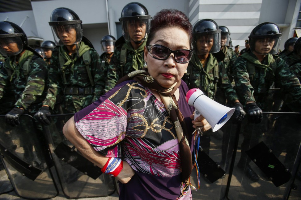 An anti-government protester stands near Thai soldiers guarding a Defence Ministry compound in north Bangkok