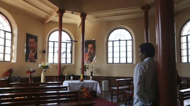 Acting Venezuelan President Maduro and his wife stand in a chapel with posters of late President Chavez in Caracas