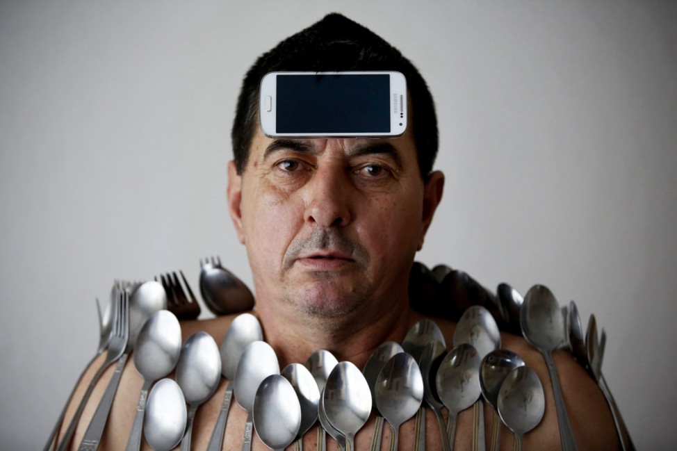 Buljubasic, 56, poses for photo with cutlery and a Samsung Galaxy S4 phone on his body and head in Srebrenik