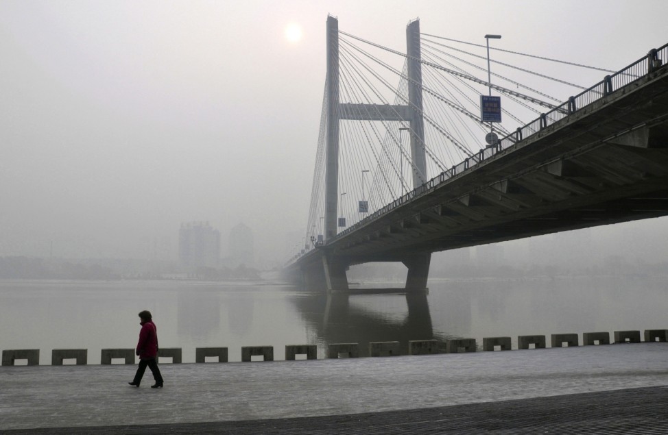 A resident walks along a street on the banks of the Songhua River near a highway bridge on a hazy day in Jilin
