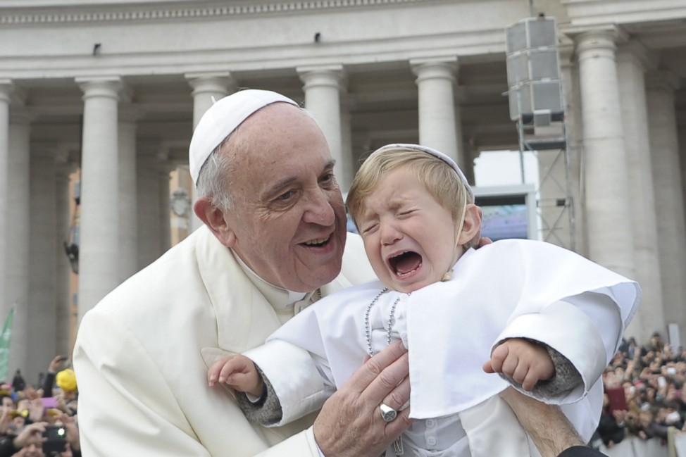 Pope Francis blesses a baby dressed as the Pope as he arrives to lead his Wednesday general audience at the Vatican