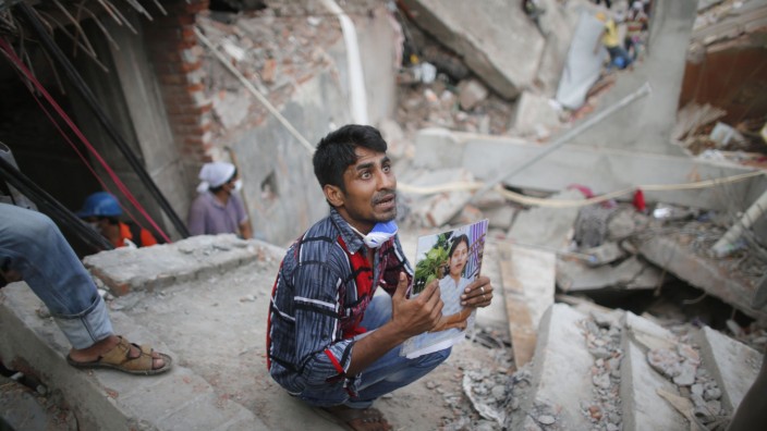 Relative holds picture of a garment worker in front of the rubble of the collapsed Rana Plaza building, in Savar