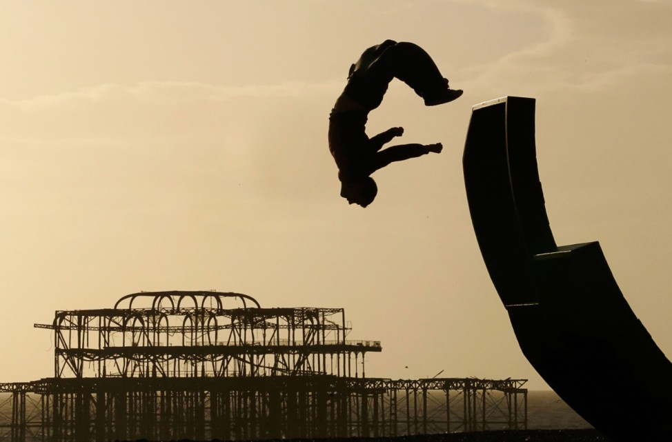 A man somersaults off a sculpture on the beach in front of the old West Pier in Brighton
