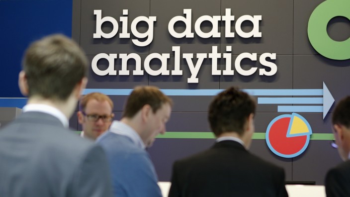 People stand in front of a big data analytics logo at the booth of IBM during preparations for the CeBIT trade fair in Hanover