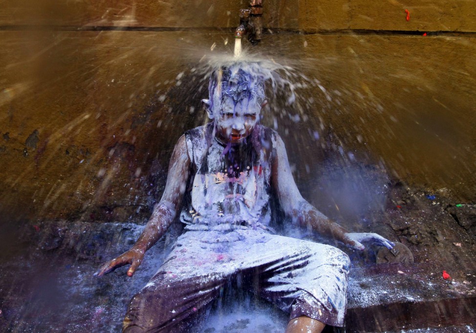 A boy sits under a water tap to wash himself after taking part in Holi celebrations in Chennai