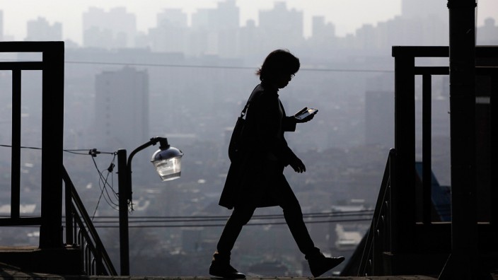 A woman uses her phone while walking on a hazy day in Seoul