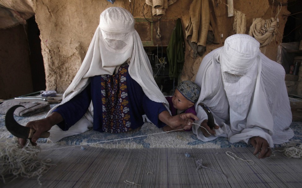 Ethnic Hazara Afghan women weave a carpet at a makeshift workshop at their house in Khorasan Refugee Camp, on the outskirts of Peshawar