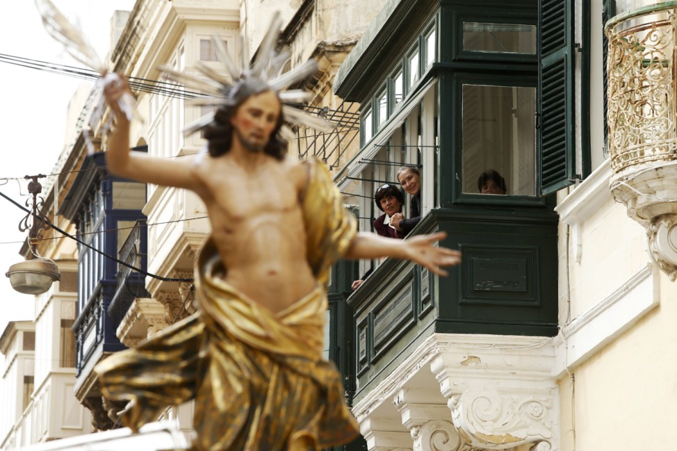 People watch from the balcony of a house as a statue of the Risen Christ is carried during an Easter Sunday procession in Cospicua