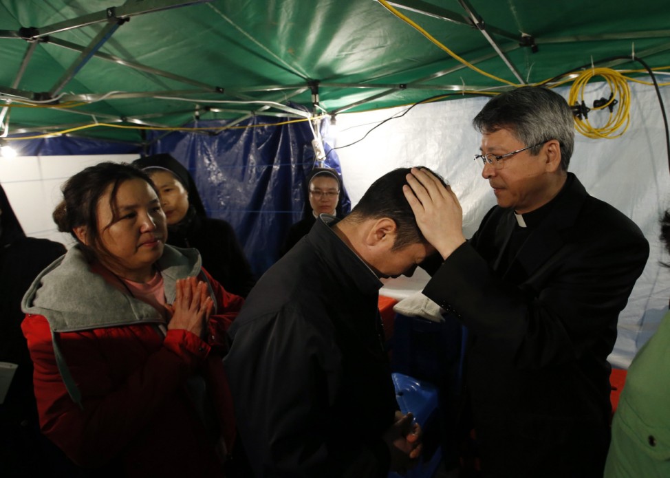 A Catholic priest prays for family members of missing passengers onboard the South Korean ferry Sewol which capsized on Wednesday, during a special Easter service  at a gymnasium in Jindo