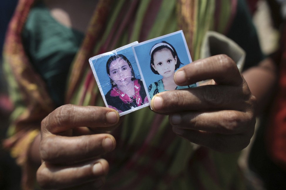 A woman holds a picture of her daughter (L), a garment worker who went missing in the Rana Plaza collapse, next to a picture of the worker's daughter on the first year anniversary of the accident, as people gather in Savar