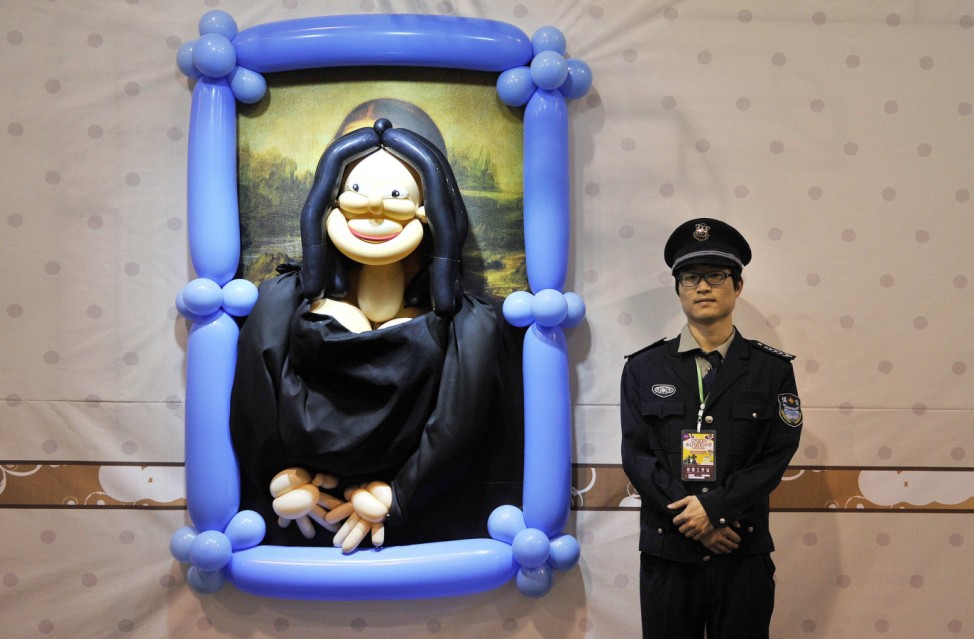 A security guard stands next to a balloon art piece depicting the painting Mona Lisa by Leonardo da Vinci at a balloon-themed carnival in Hefei
