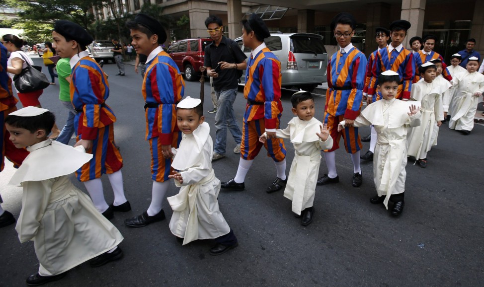 Children wearing Pope's cassocks cross a road before taking part in a parade in Quezon city