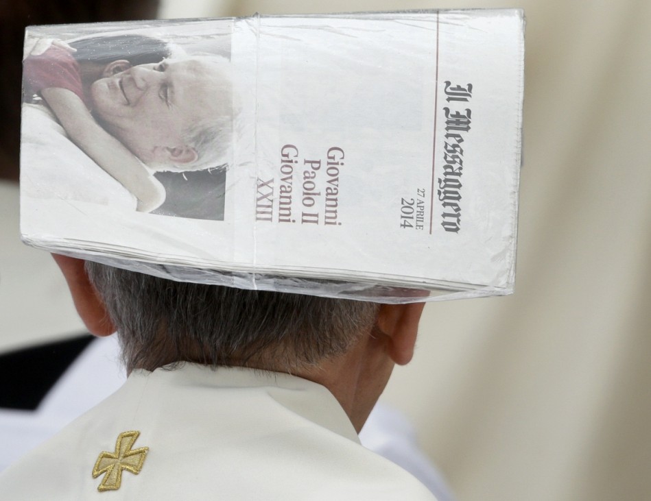 A priest covers his head with a newspaper during rainfall ahead of the canonisation ceremony of Popes John XXIII and John Paul II in St. Peter's Square at the Vatican
