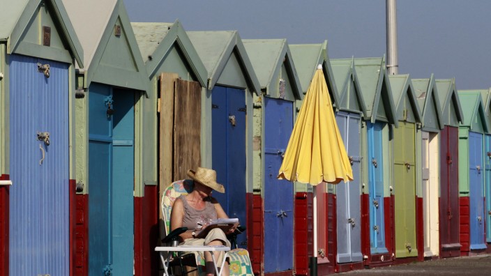 A woman reads as she sits outside a beach hut in Brighton, southern England