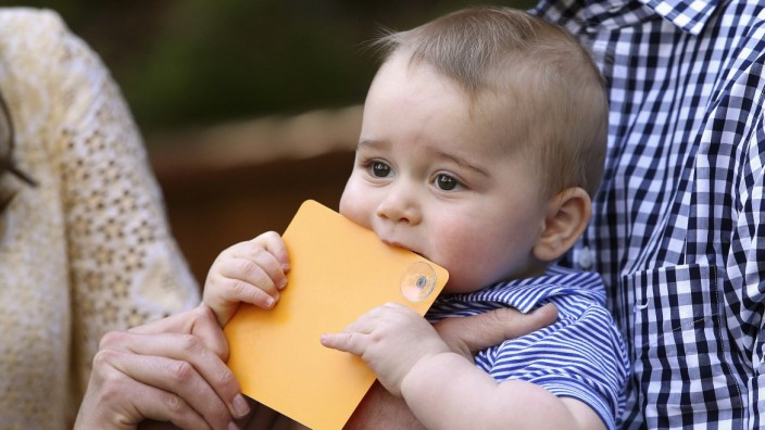 Britain's Prince George chews on a commemorative card given to him by his mother Catherine, Duchess of Cambridge, as he is held by his father Prince William at Bilby Enclosure in Taronga Zoo in Sydney