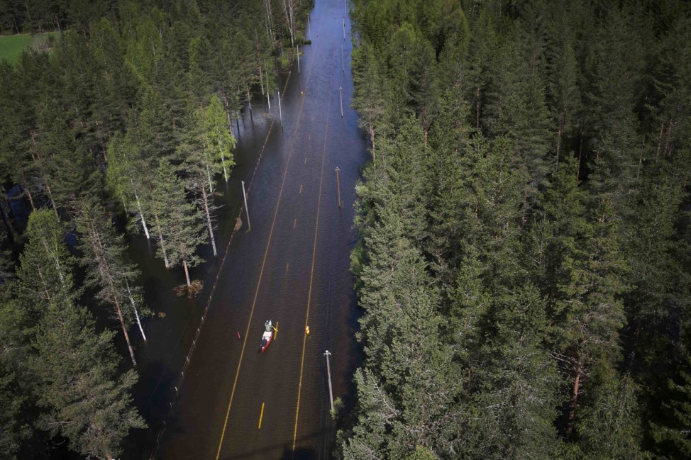 Two men paddle in a canoe on a flooded road in Trysil