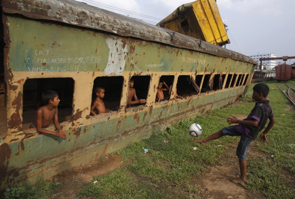 Children play football in front of an abandoned train compartment next to a railway track in Dhaka