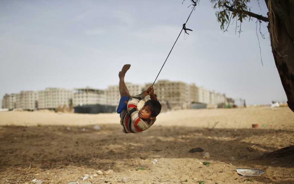 A Palestinian boy swings on a rope tied on a tree at a former Jewish settlement in Khan Younis in the southern Gaza Strip