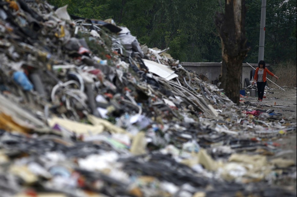 A woman walks near mounds of garbage, which were abandoned by recycling workers, at Dongxiaokou village in Beijing