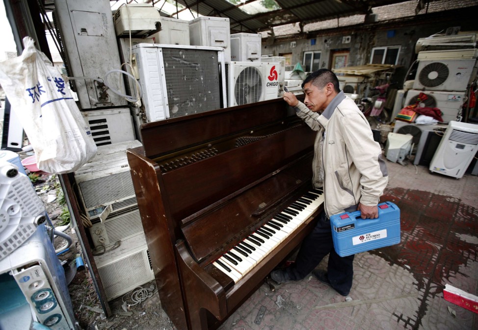 A recycling worker looks at a broken piano in the yard of a tenement house at Dongxiaokou village in Beijing