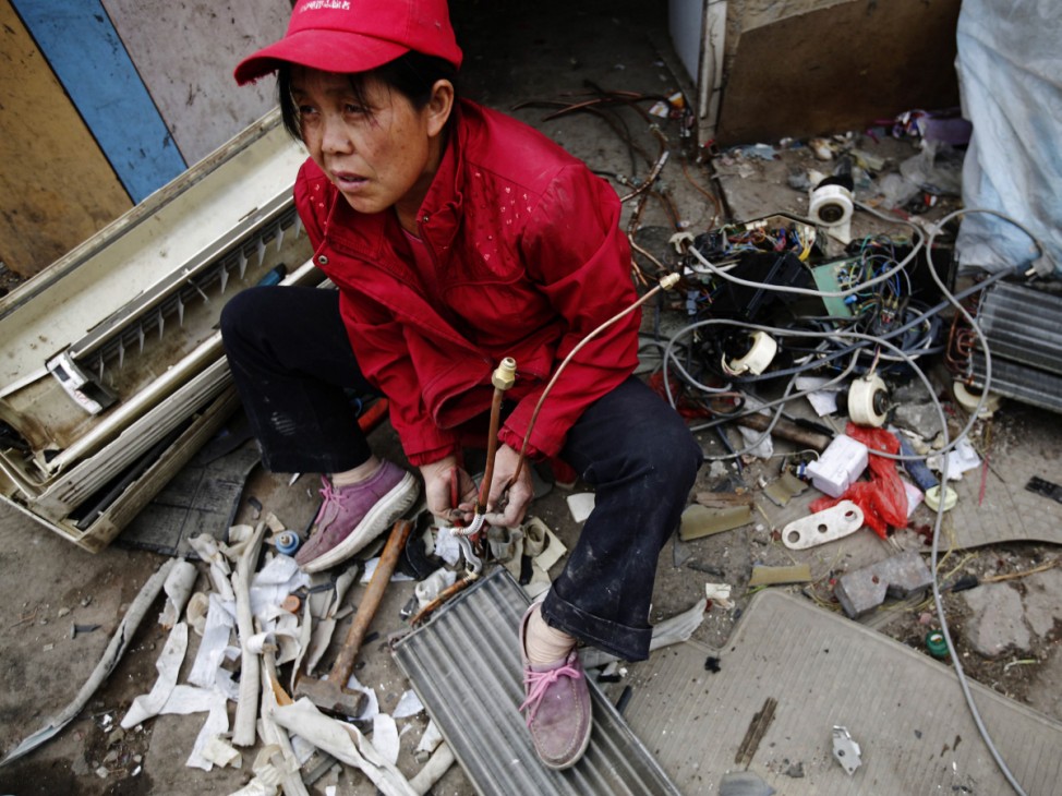 A woman dismantles a broken air-conditioning unit to sell its parts as scrap, outside a tenement house at Dongxiaokou village in Beijing