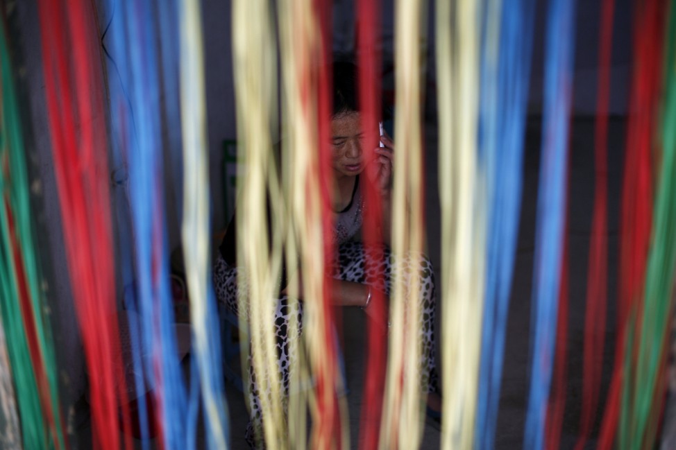 Recycling worker Gu Zhaofang is seen behind a blind as she speaks on her mobile phone at her tenement house at Dongxiaokou village in Beijing
