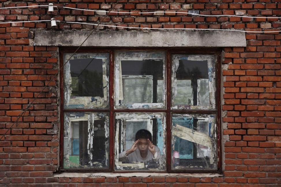 A boy looks out a window at a school, which is attended by recycling workers' children, in Dongxiaokou village in Beijing