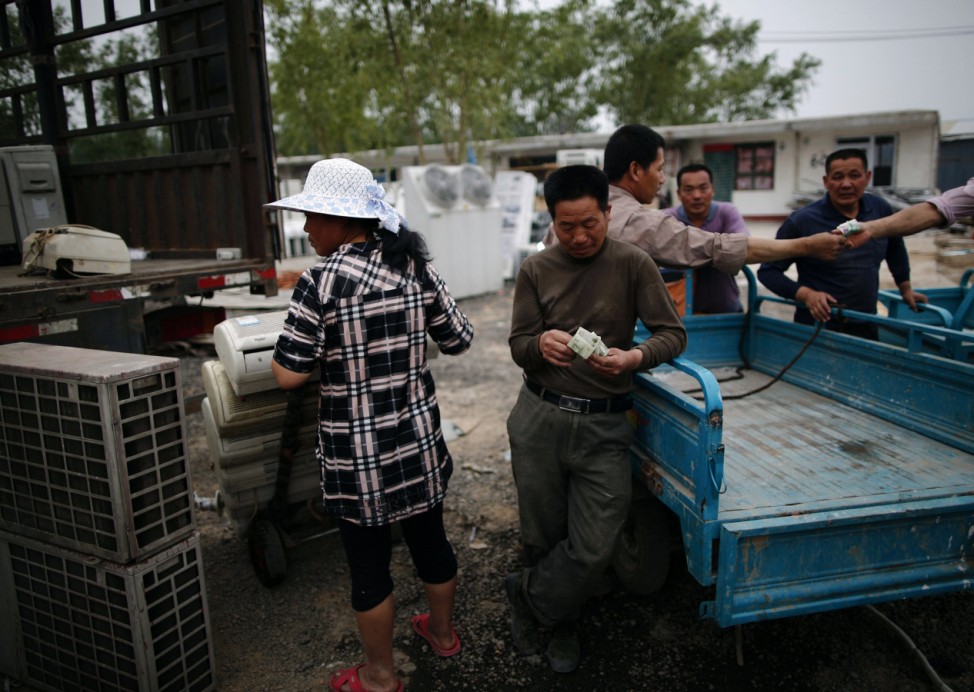 A man counts his money after selling recycled air-conditioning units to a vendor in the yard of a tenement house at Dongxiaokou village in Beijing