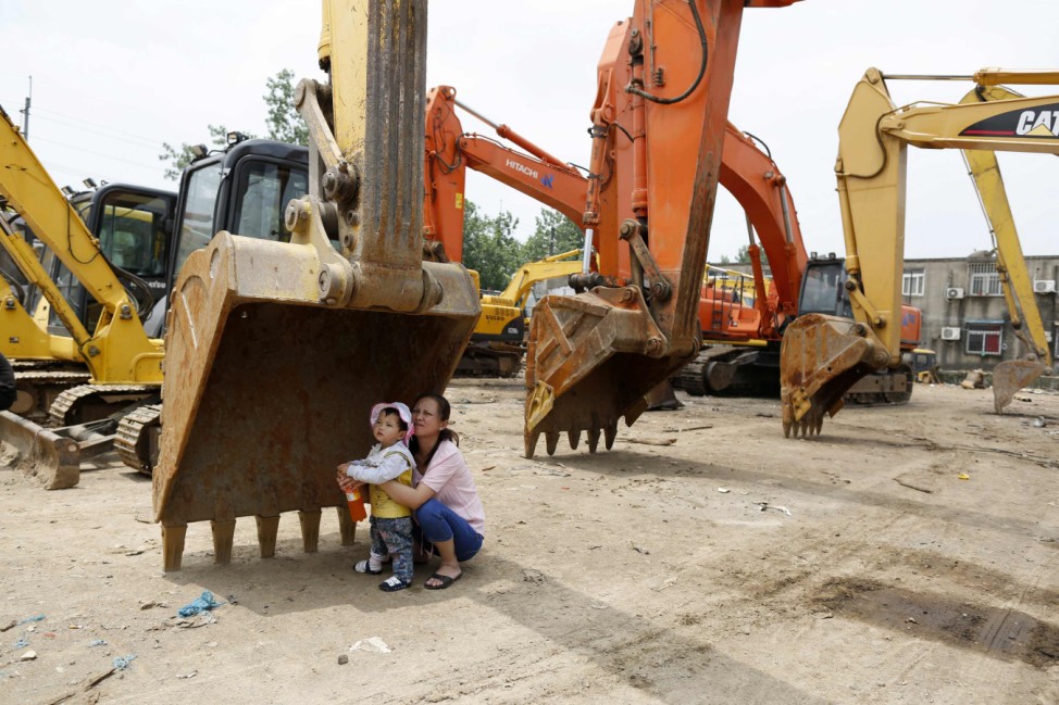 A mother rests with her child in the shade at a machinery maintenance station in Shanghai