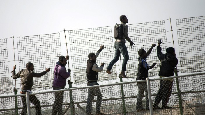African migrants climb a border fence covered in razor wire between Morocco and Spain's north African enclave of Melilla