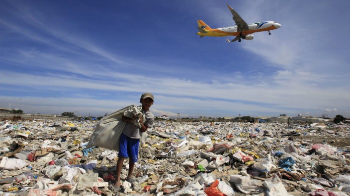 An aircraft flies overhead as a person rummages for recyclables at a garbage dumpsite in Paranaque city