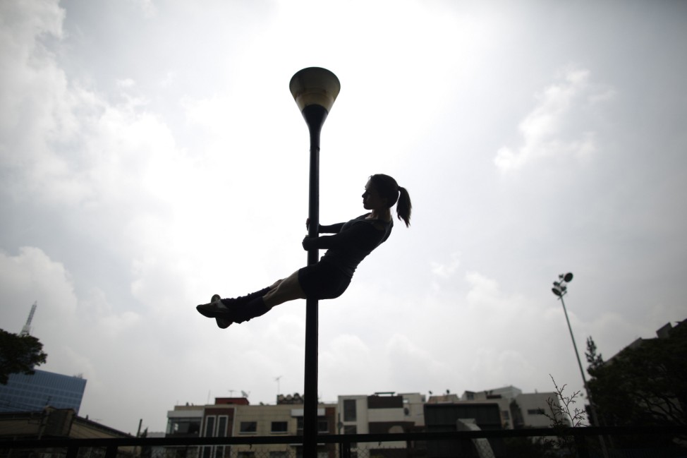 Woman performs a pole dancing routine on a lamp post during the national day celebration of 'Urban Pole' dance at a park in Mexico City
