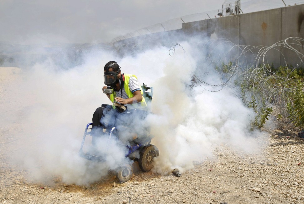 A disabled Palestinian protester moves away from tear gas fired by Israeli troops during a protest in solidarity with hunger-striking Palestinian prisoners held by Israel, in Bilin