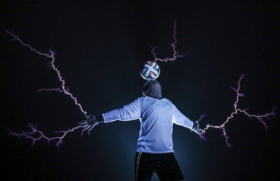 Member of Thunderbolt Craziness band wearing a metal suit balances a soccer ball on his head as electricity is discharged from Tesla coils during a performance to celebrate 2014 Brazil World Cup, in Changle
