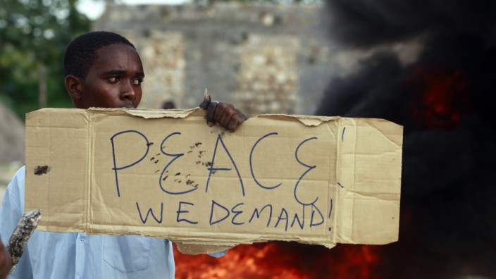 A resident holds a placard as he participates in a protest against the recent attack by unidentified gunmen in the coastal Kenyan town of Mpeketoni