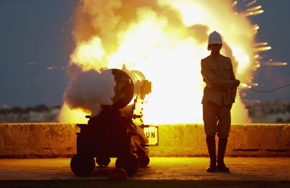 A National Heritage Trust historical re-enactor in Victorian-era Royal Malta Artillery uniform fires cannon during feast day of Saint John the Baptist on bastions of Valletta