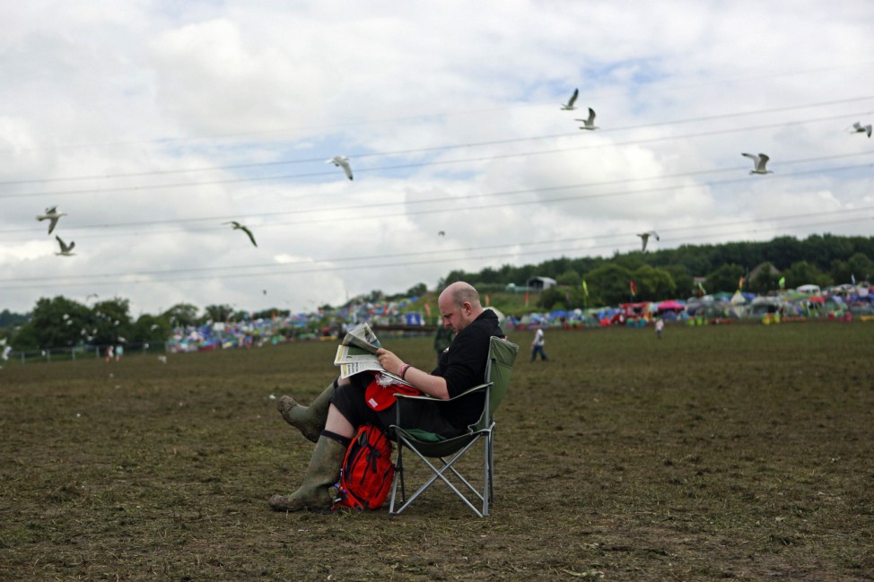 A festival goer reads the paper in front of the Pyramid stage at Worthy Farm in Somerset, during the Glastonbury Festival