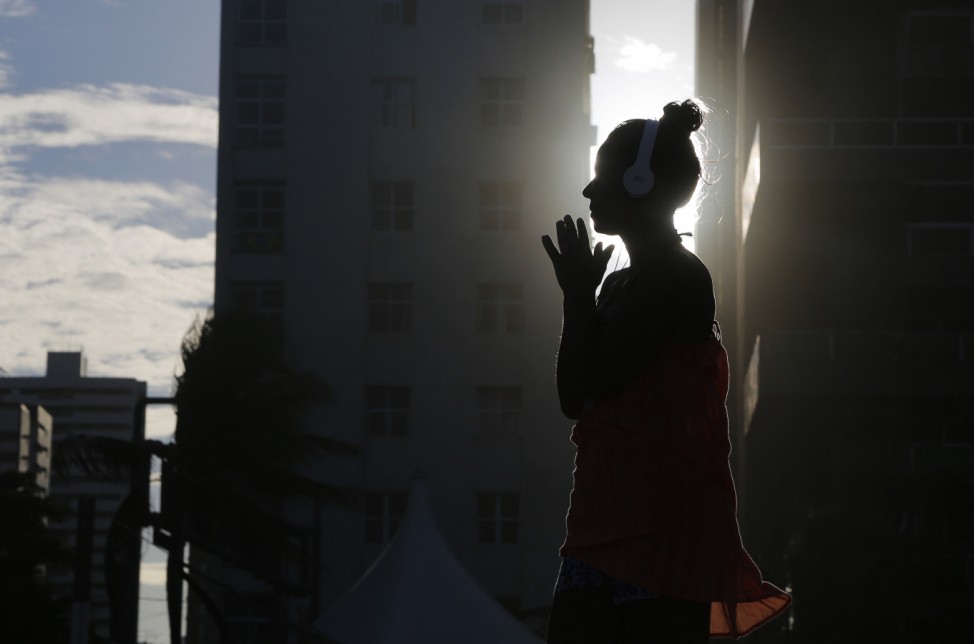 A woman listens to music as the sun sets as seen between buildings on Boa Viagem beach in Recife