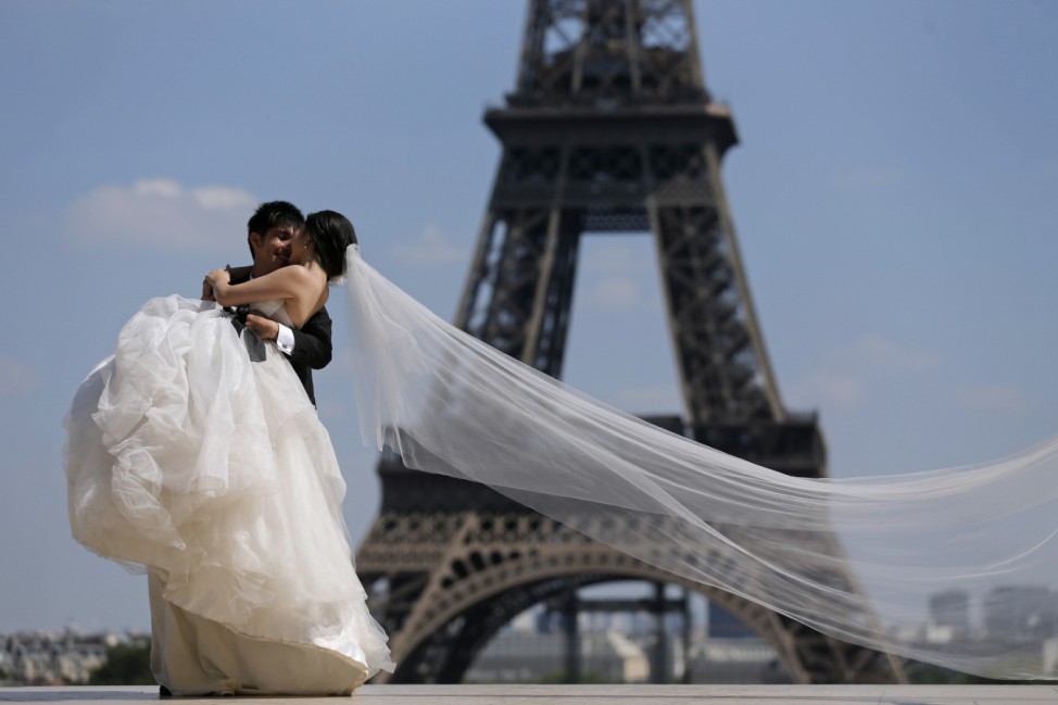 A wedding couple of tourists pose for their own photographer at the Trocadero Square near the Eiffel Tower in Paris