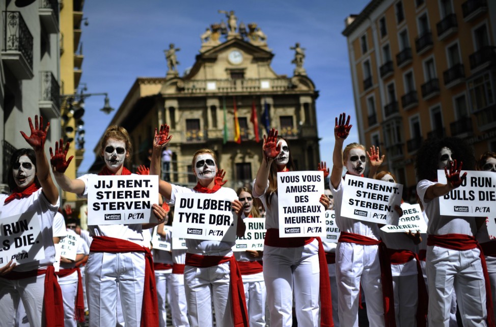 Anti-bullfighting protesters wearing skull make-up and traditional red scarves hold up signs that read, 'You Run. Bulls Die', during a demonstration in front of Pamplona town hall