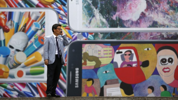 A man uses his mobile phone in front of a giant advertisement promoting Samsung Electronics' new Galaxy S5 smartphone, at an art hall in central Seoul