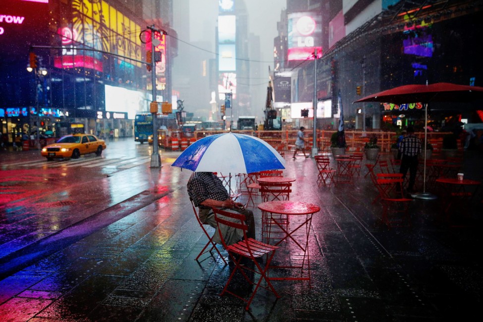 A man sits with an umbrella during a rainstorm at Times Square in New York