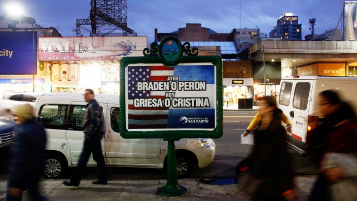 People walk past a poster placed on an advertising board that reads 'Yesterday, Braden or Peron - Today: Griesa or Cristina', in Buenos